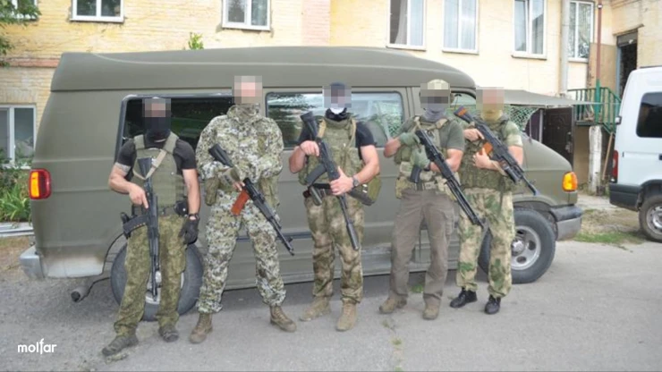 People with weapons in camouflage against the background of a khaki minibus