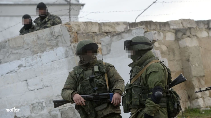 Two armed men in Russian military uniforms against a wall