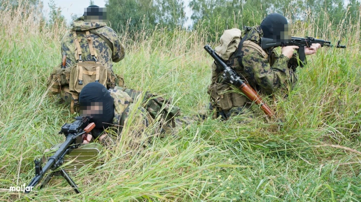 Three armed men in camouflage and balaclavas in the grass