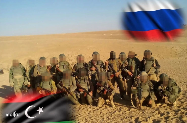 A group of armed men in the desert with the flags of Libya and Russia in the corners of the picture